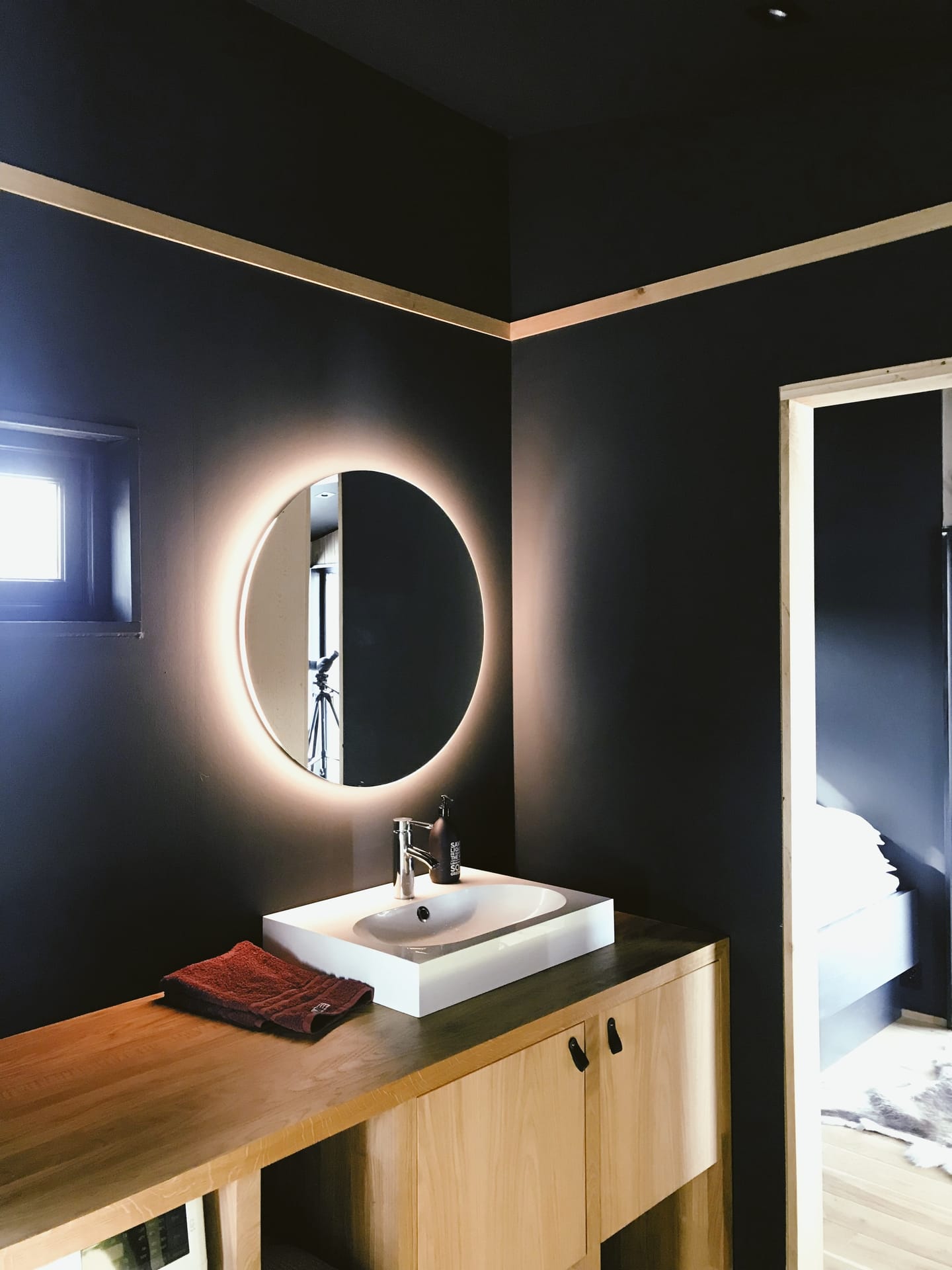 A round backlit mirror illuminating a dark bathroom
